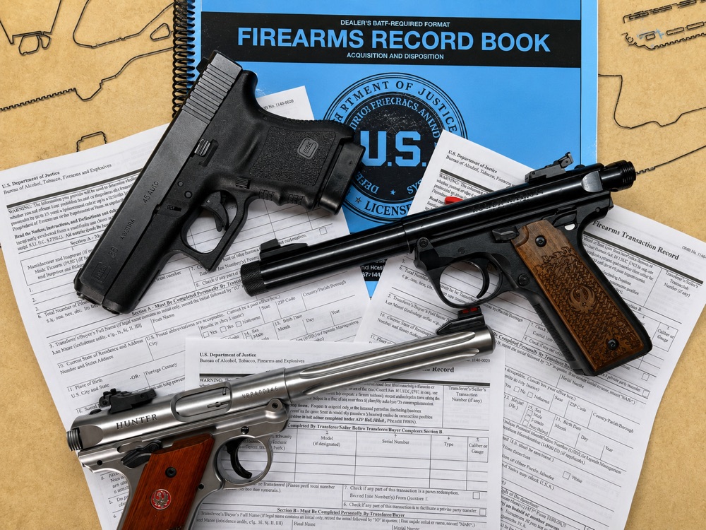 Handguns laid on completed ATF Form 4473 firearms transaction records and a dealer Firearms Record Book at Bossert's Military Surplus, the paperwork side of an FFL transfer.